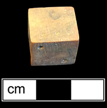 Unfinished bone die.  This example is one of seven unfinished dice or game pieces recovered from this privy.  The die has been shaped and markings made for the placement of the dots, for later drilling.  Each of the pieces has split or shows damage that led to its being discarded before completion. 18BC80