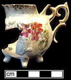 Porcelain teapot sized for a child. Molded with upright flowers appearing to be irises, but printed and painted over the glaze and over the molding with a wild rose motif. Gold gilt painting on handle and feet and sponging on rim.  Base of vessel has enameler’s mark number 712 painted in gold. Impressed number “1648” on base.