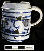 Gray-bodied salt glazed stoneware straight-sided tankard  with applied AR medallion and engraved (incised) foliage outlined in cobalt-blue under the glaze. Cordoned rim. This medallion stands for British monarch Queen Anne (1702-1714).  Vessel date 1702-1714, from 44YO205 John Bates Site. Photo courtesy of the Colonial Williamsburg Foundation.&nbsp;Artifacts from private collection.