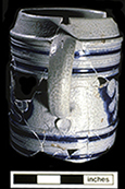 Gray-bodied salt glazed stoneware straight-sided tankard  with applied AR medallion and engraved (incised) foliage outlined in cobalt-blue under the glaze. Cordoned rim. This medallion stands for British monarch Queen Anne (1702-1714).  Vessel date 1702-1714, from 44YO205 John Bates Site. Photo courtesy of the Colonial Williamsburg Foundation.&nbsp;Artifacts from private collection.