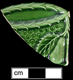 Green glazed scalloped rim plate with fruit and foliage flange design.  The green glaze was developed by Josiah Wedgwood in 1759 (Noel Hume 2001:205). Possibly produced by the Swinton Pottery, circa 1770s (Cox 2005:119).