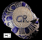 Gray-bodied salt glazed stoneware jug with applied round medallion molded with crowned GR cipher of King George I (1714-1727) or King George II (1727-1760). Just to the right of the angel&rsquo;s wings are the initials SW (see detail).  The initials together on the right hand side in this manner generally indicate a 2 quart jug. Skerry and Hood (2009:50) date these SW marked jugs to the period between 1715 and 1740. Vessel 2317, from 18PR175.