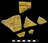 North Devon sgraffito dish with incised probably floral motif. White slip over red and grey earthenware body, with lead glazed interior - QV87.