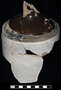 North American buff bodied stoneware jug with Albany slipped shoulder, neck and handle. Bristol glaze covers the cylindrical body. Damaged by burning. Vessel diameter: 6.00”, Vessel V-17 from 18MO609.