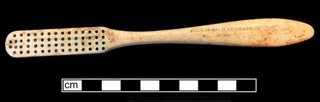 Bone handle with teardrop shape toothbrush with wire drawn attachment and copper alloy staining on back. Stamped on front: “England” near stock and “Hochschild Kohn & Co. Baltimore” and “Drawn Wire/Sterling/Silver Wire” on handle. 18BC92