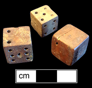 Unfinished bone die.  This example is one of seven unfinished dice or game pieces recovered from this privy.  The die has been shaped and markings made for the placement of the dots, for later drilling.  Each of the pieces has split or shows damage that led to its being discarded before completion. 18BC80